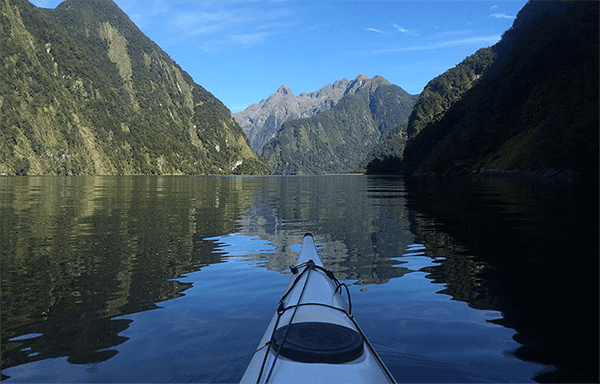 Paddlers view over the front end of a sea kayak looking out over the water and mountains of Doubtful Sound
